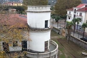 A white cylindrical tower with a balcony, surrounded by a stone wall and palm trees. - B&B Veronica (Baronissi)