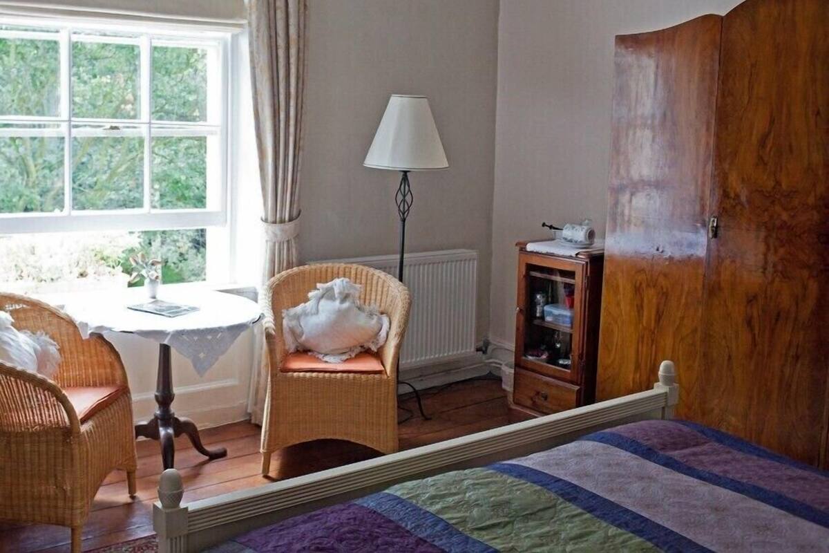 Ein Schlafzimmer mit einem Bett, einem Sessel, einem kleinen Tisch, einer Lampe und einem Holzschrank.