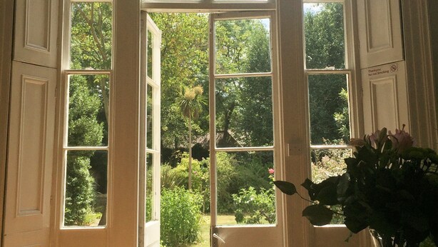 A room with a large bay window, a table with books and a vase of flowers, and a door with a "No Smoking" sign. - Temple Lodge Club (London)