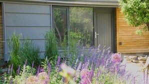 A house with a grey exterior, a wooden door, and a garden with various plants and flowers. - Temple Lodge Club (London)
