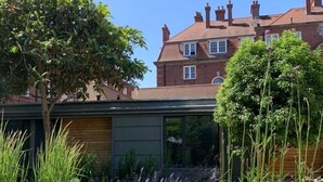 A residential garden with a pathway, various plants, and a brick house in the background. - Temple Lodge Club (London)
