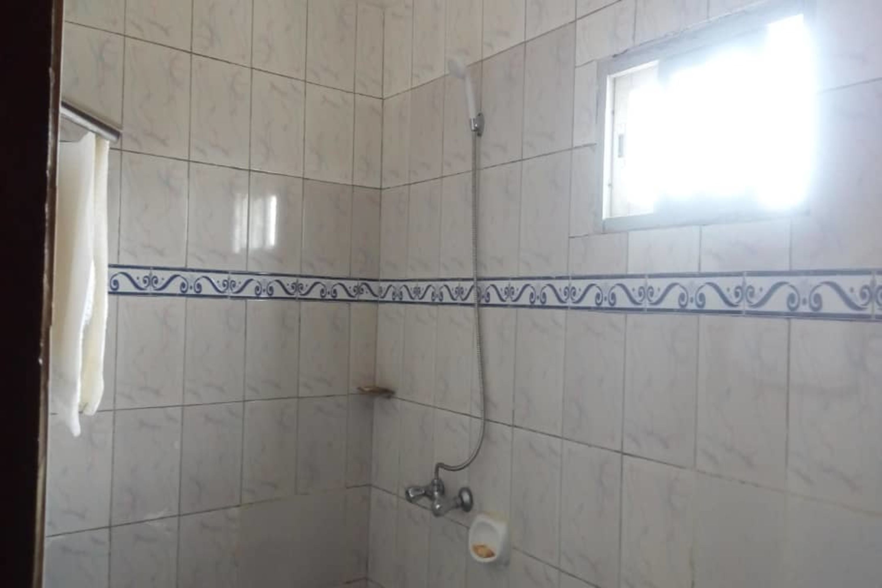 A bathroom with white tiles, a shower, and a window.