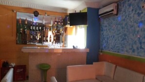 A bar area with a counter, stools, and a seating area with a couch and a table. - Hotel Kama (Abidjan)