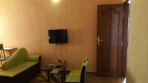 A living room with a green sofa, a black chair, a small table, and a television mounted on the wall. - Hotel Kama (Abidjan)