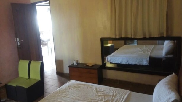 A bedroom with a bed, a nightstand, a chair, and a mirror. - Hotel Kama (Abidjan)