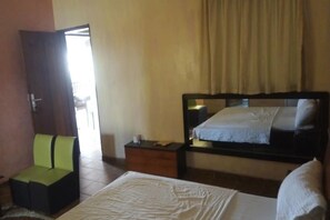 A bedroom with a bed, a nightstand, a chair, and a mirror. - Hotel Kama (Abidjan)