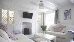 Ein weiß gestrichenes Wohnzimmer mit Kamin, einer Couch, einem Couchtisch und einem an der Wand befestigten Fernseher.