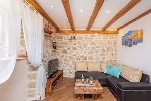 Ein gemütliches Wohnzimmer mit Steinwand, Holzbalken, einem schwarzen Sofa und einem Couchtisch mit Dekoration.