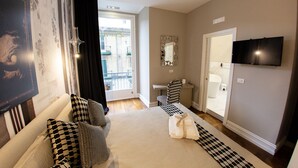 A hotel room with a bed, a checkered chair, a TV, a mirror, and a view of the outside balcony. - Leone Camere D'Autore (Naples)
