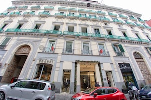 Un edificio a più piani con architettura classica, caratterizzato da un ingresso a livello strada con un'ampia porta ad arco e un'insegna con scritto “BRAND”.