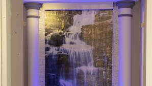 A water feature with a waterfall and illuminated blue lighting, framed by columns. - Leone Camere D'Autore (Naples)
