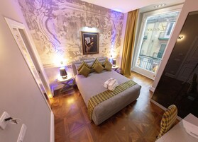 Una camera d'albergo con un letto grande, un comodino con una lampada, vista sulla città attraverso una finestra e una parete decorativa.