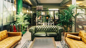Una sala de estar acogedora con un sofá de cuero verde, dos sillones amarillos, una mesita de centro y una estantería llena de libros y plantas.