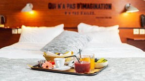 Una cama impecablemente hecha con una bandeja de desayuno que incluye una bebida, un cuenco de fruta y un tarro pequeño.