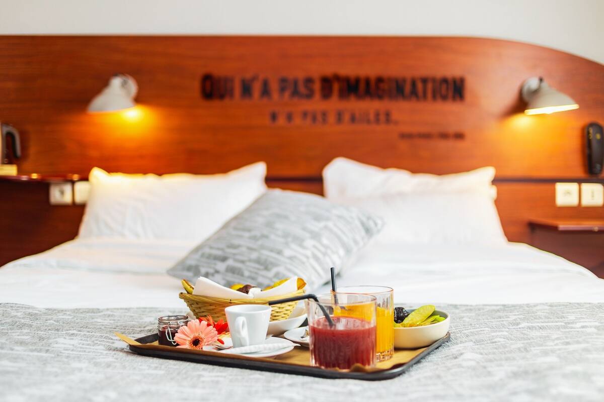 A neatly made bed with a tray of breakfast items including a drink, a bowl of fruit, and a small jar.