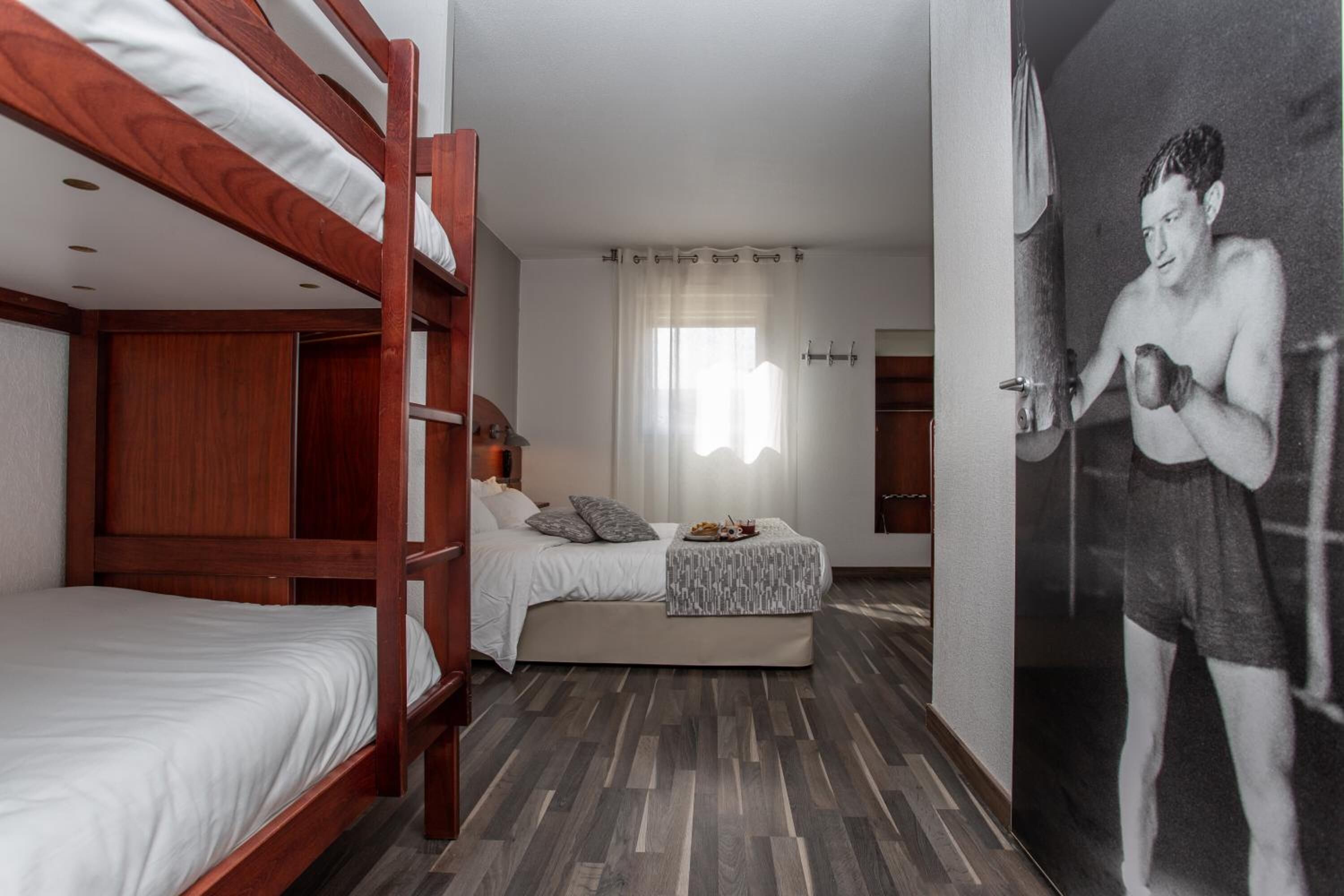 A room with bunk beds, a bed with a patterned blanket, a wall-mounted picture, and a wooden floor.