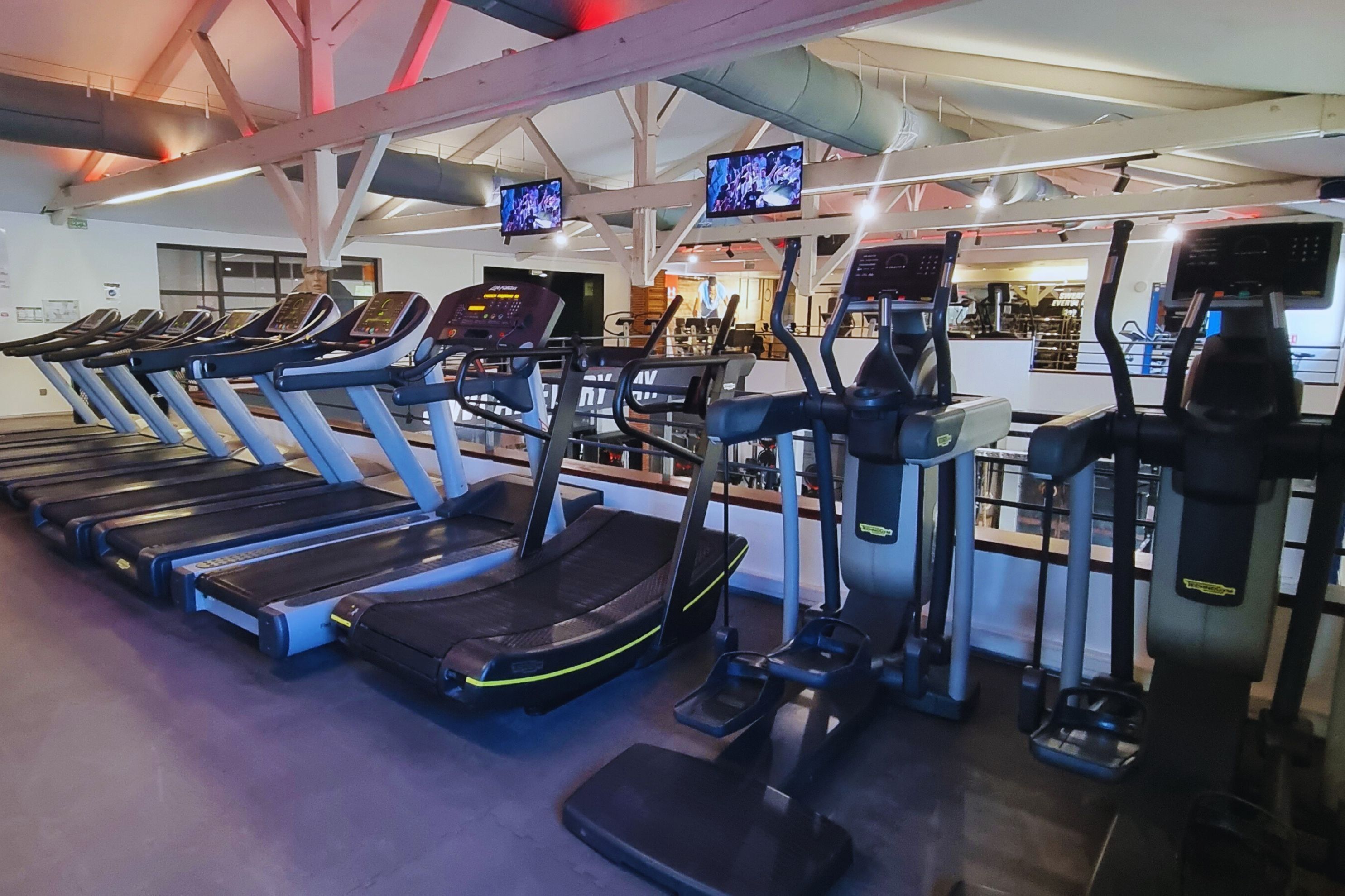 Un gimnasio con cintas de correr, elípticas y una banca de pesas.