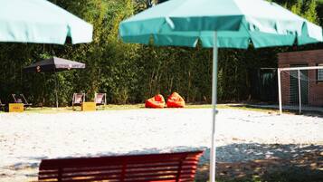 A sandy outdoor area with two green umbrellas, a red bench, and two orange bean bags.