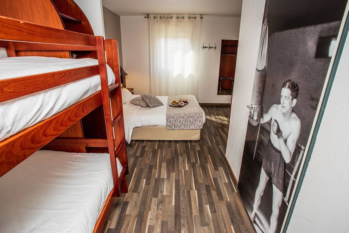 A room with bunk beds, a small sofa, a table with snacks, and a poster on the wall.