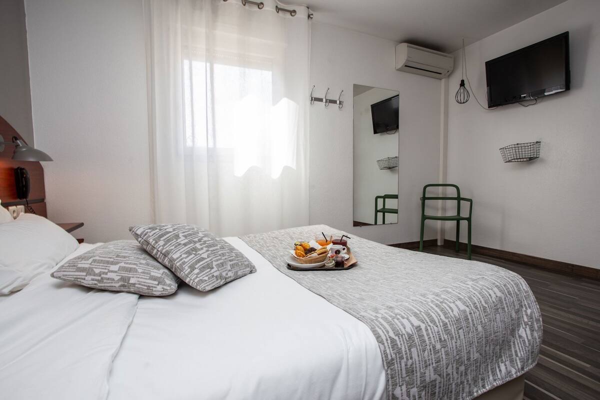A hotel room with a bed, a breakfast tray, a green chair, a TV, and a mirror.
