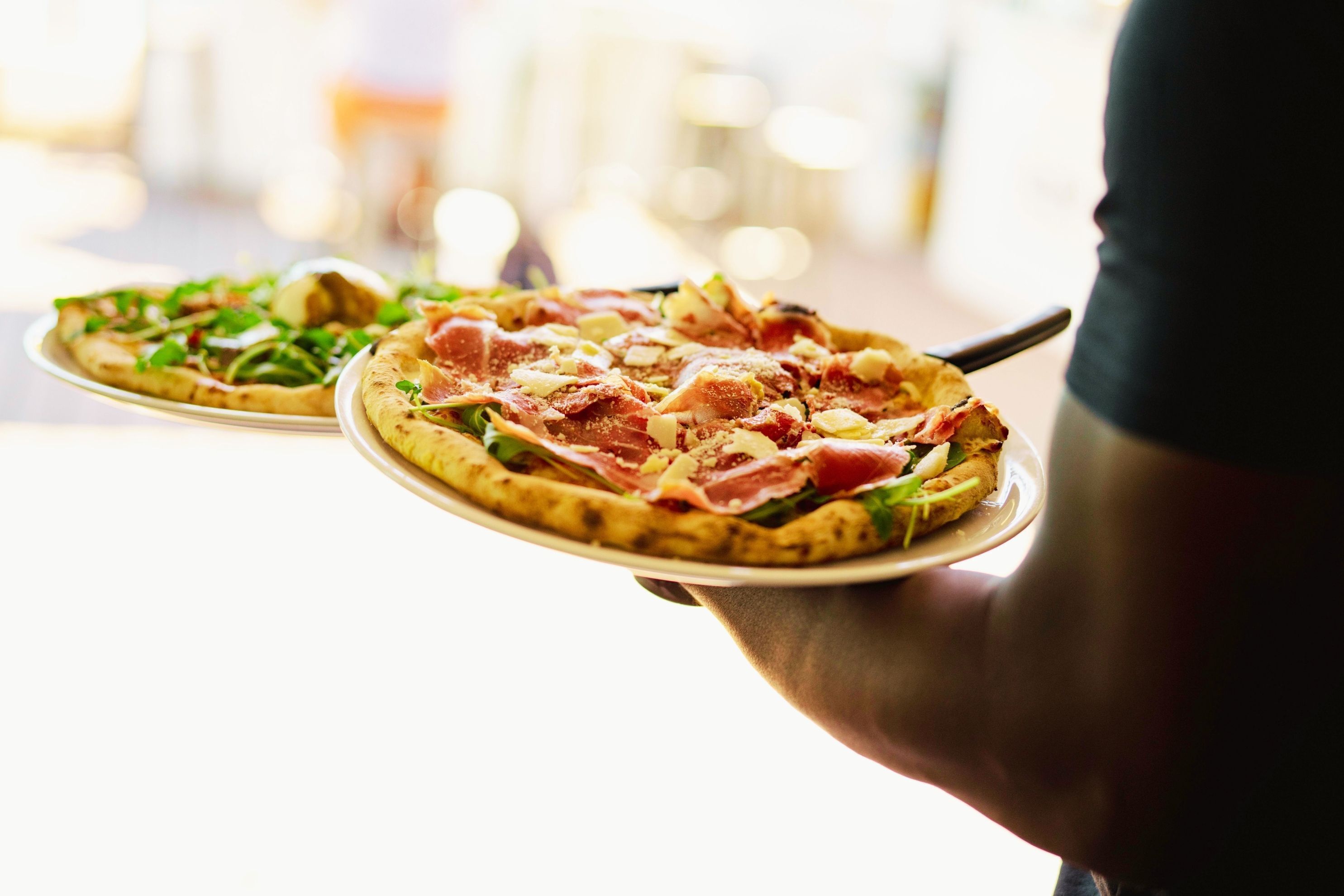 A person holding two pizzas with different toppings.