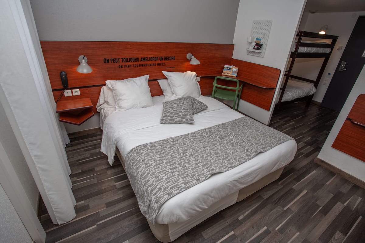 A hotel room with a large bed, bedside tables, a green chair, and a bunk bed in the corner.