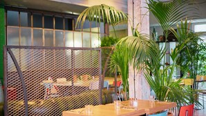 Un restaurante con una mesa de madera, sillas y un separador de malla.