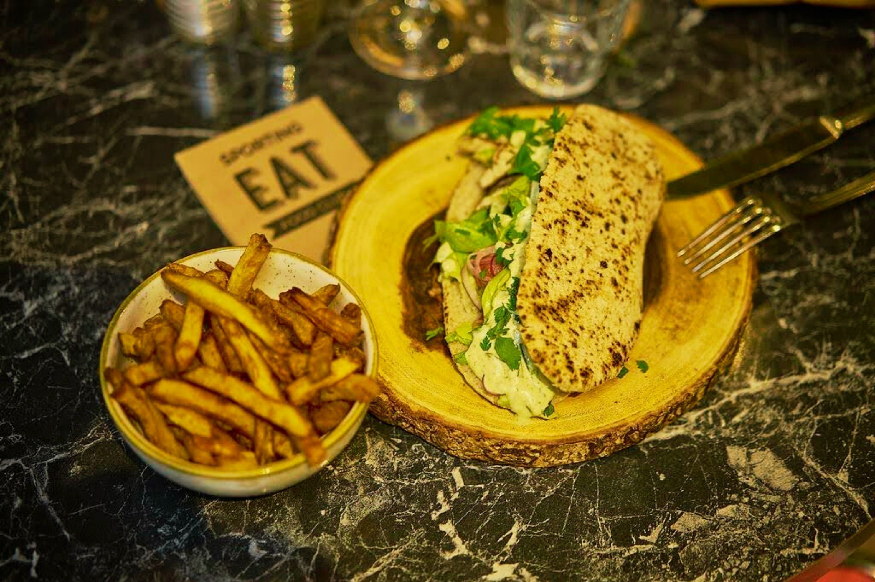 A sandwich on a wooden board with a side of fries, and a sign that reads "EAT".