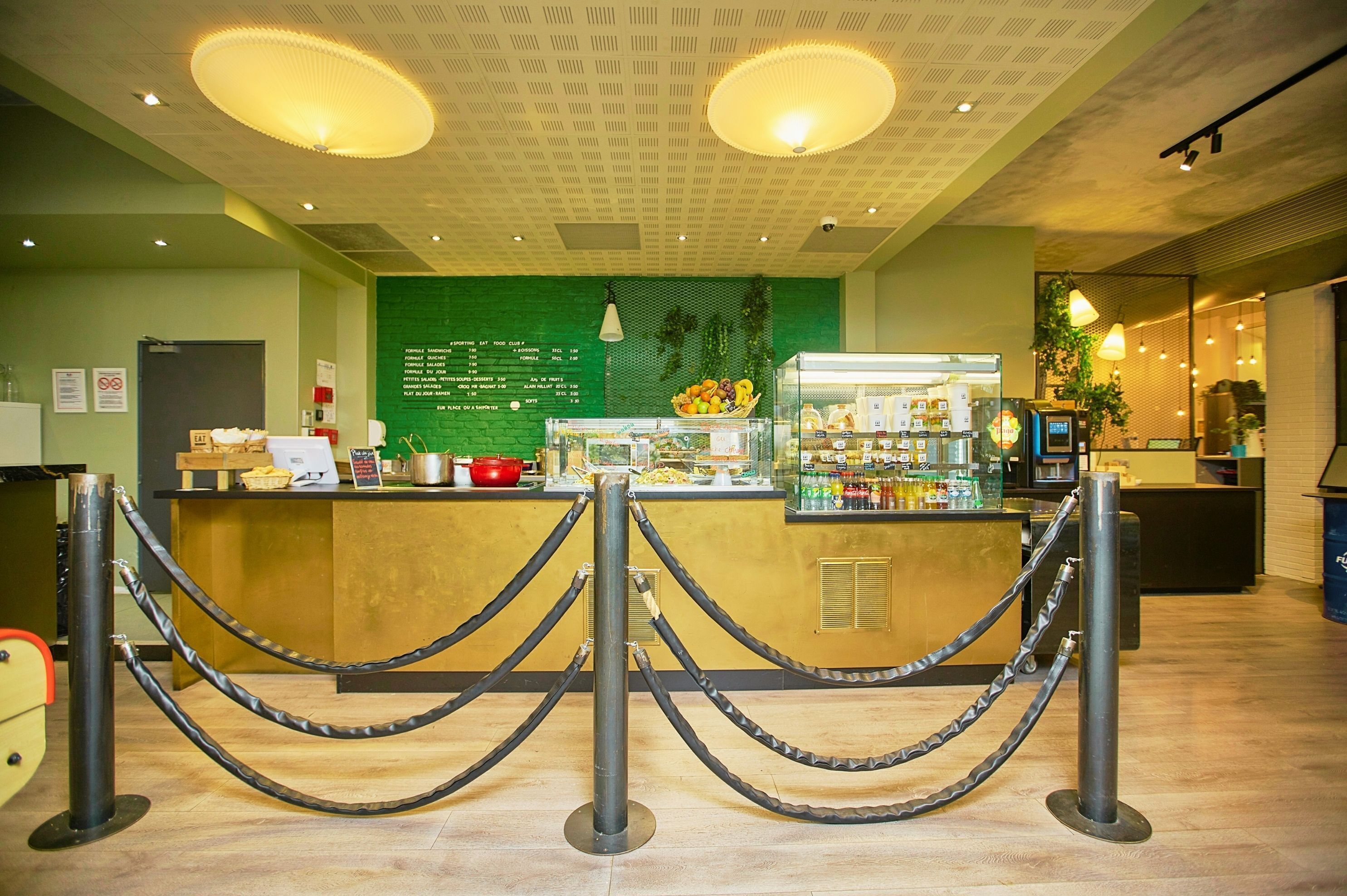Zona de recepción con un muro verde que muestra un menú, una barra con diferentes opciones de comida y una máquina de café.