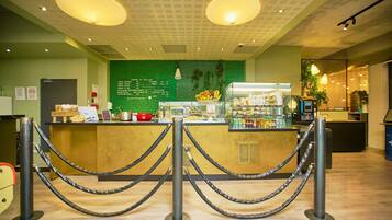 Zona de recepción con un muro verde que muestra un menú, una barra con diferentes opciones de comida y una máquina de café.