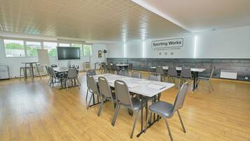 A spacious conference room with multiple tables and chairs, a large flat-screen TV, and a sign for 'Sporting Works' seminars and coworking.