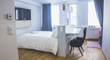 Un dormitorio moderno con cama, escritorio, silla y ventana con cortinas.