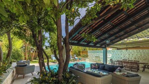 Une terrasse extérieure avec des meubles en osier, une piscine et un mur en pierre.