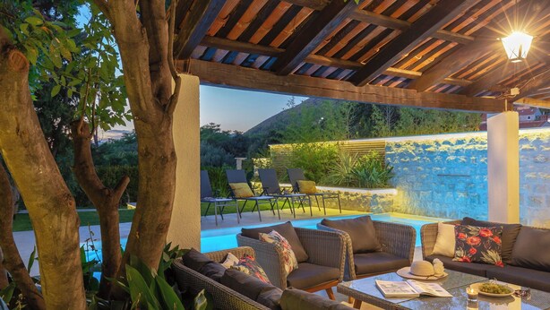 Une terrasse extérieure avec des meubles en osier, une piscine et un mur en pierre.