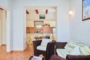A compact living space with a kitchenette, wicker furniture, and a painting on the wall. - Apartment Fresco - Two Bedroom Apartment, Sleeps 4 (Dubrovnik)