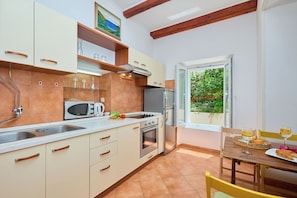 A kitchen with a sink, microwave, stove, and refrigerator. There is a window with a view of greenery outside. - Apartment Fresco - Two Bedroom Apartment, Sleeps 4 (Dubrovnik)