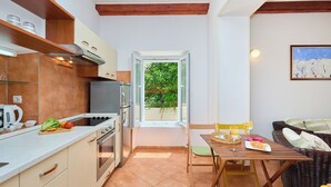 A compact kitchen with modern appliances, a dining area with a table and chairs, and a view of greenery through a glass door.