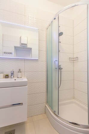 A modern bathroom with a glass-enclosed shower, a white vanity with a mirror, and a small shelf with toiletries. - Hedera Estate, Villa Hedera V (Dubrovnik)