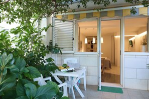 Uma área de refeições ao ar livre com uma mesa, cadeiras, uma janela com persianas e uma porta que dá para o interior.