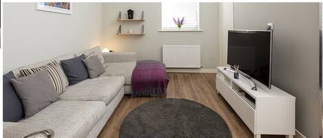 A living room with a grey sofa, a white TV stand, and a large flat-screen TV.