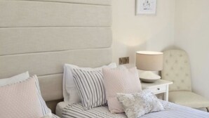 A neatly arranged bedroom with a bed, pillows, a bedside table, and a chair. - The Lane Apartment (Edinburgh)
