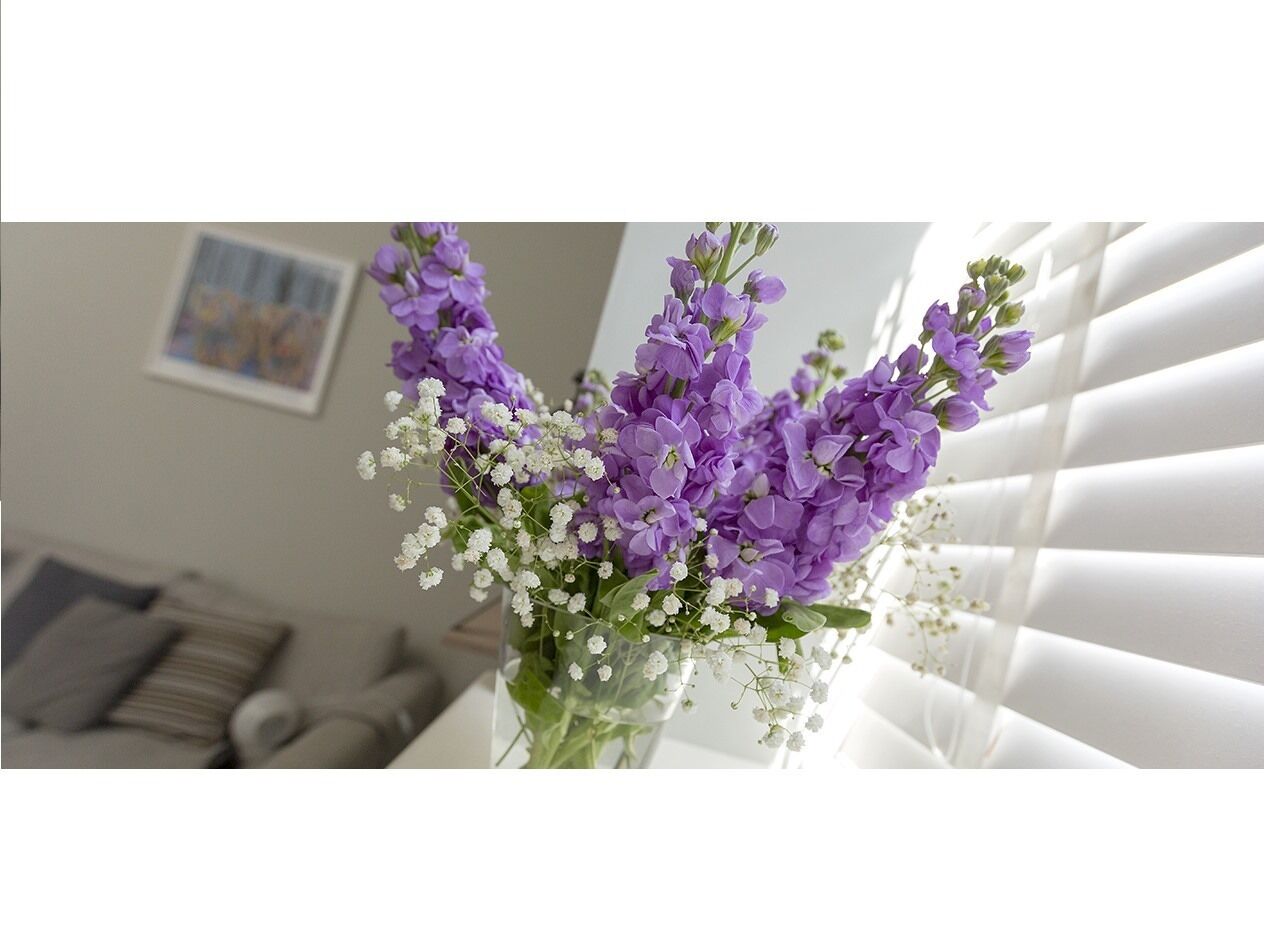 Eine Vase mit violetten Blumen und weißen Trockenblumen auf einem Tisch.