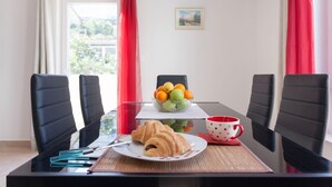 A dining table with a plate of croissants, a bowl of fruit, and a polka-dotted cup.