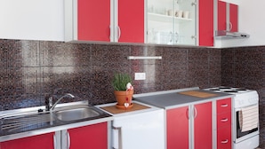 A kitchen with red cabinets, a stainless steel sink, and a tiled backsplash.