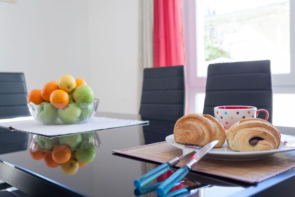 A table with a fruit bowl, croissants, a cup, and a knife.
