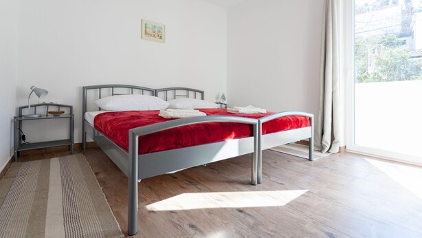 A modern bedroom with a metal bed frame, white bedding, and a view of the city through a large window.