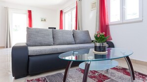 A modern living room with a grey sofa, a glass coffee table, and a red and grey patterned rug.