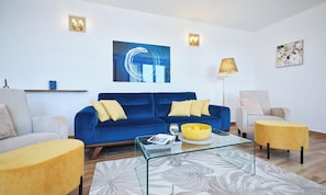 A living room with a blue sofa, two armchairs, a glass coffee table, and a floor lamp.