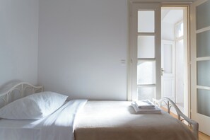 A room with a bed, white walls, and a door leading to another room.