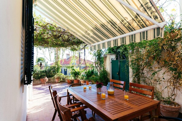 An outdoor patio with a wooden table and chairs, potted plants, and a green wall.